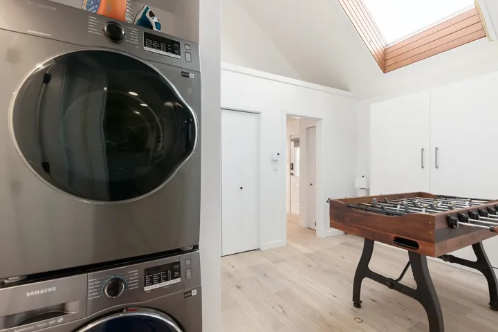 Laundry area with light wood-style floors, a skylight, vaulted ceiling, and stacked washer and clothes dryer