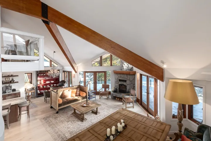 Living room with a fireplace, vaulted ceiling, light wood-style floors, and french doors