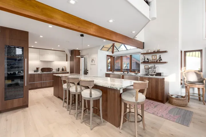 Kitchen with modern cabinets, beam ceiling, light stone countertops, two tone cabinetry, and light wood finished floors