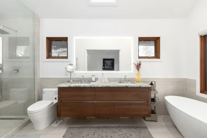 Bathroom featuring tile walls, wainscoting, double vanity, a stall shower, and a soaking tub