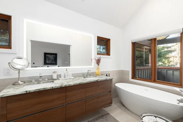 Bathroom featuring a freestanding bath, double vanity, lofted ceiling, tile walls, and a wainscoted wall
