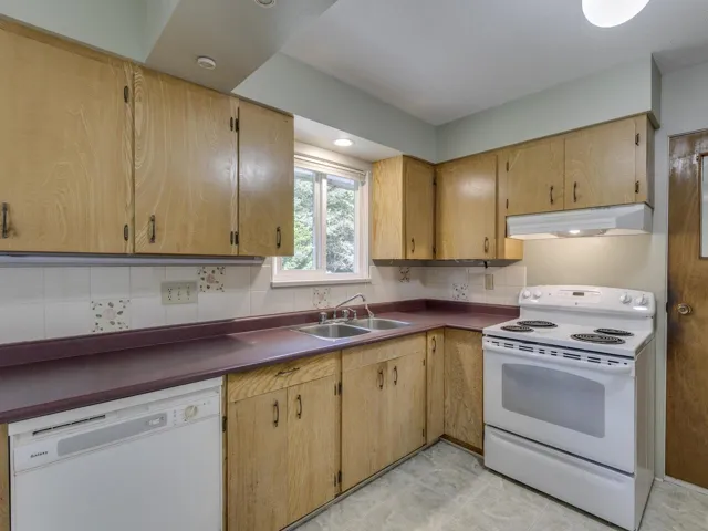 Kitchen with white appliances, under cabinet range hood, dark countertops, backsplash, and recessed lighting