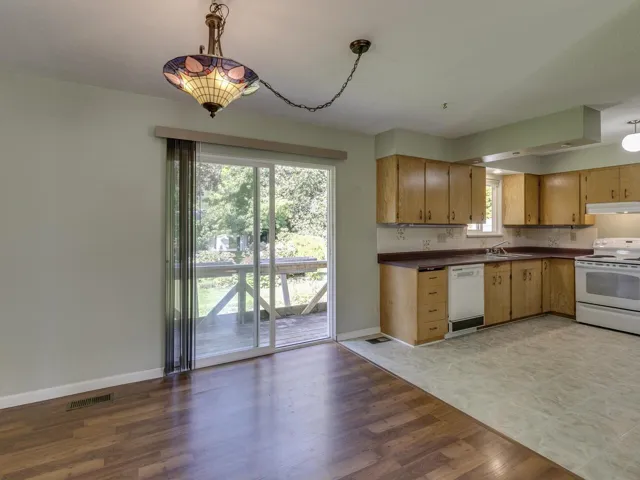 Kitchen featuring white appliances, pendant lighting, light wood finished floors, tasteful backsplash, and dark countertops