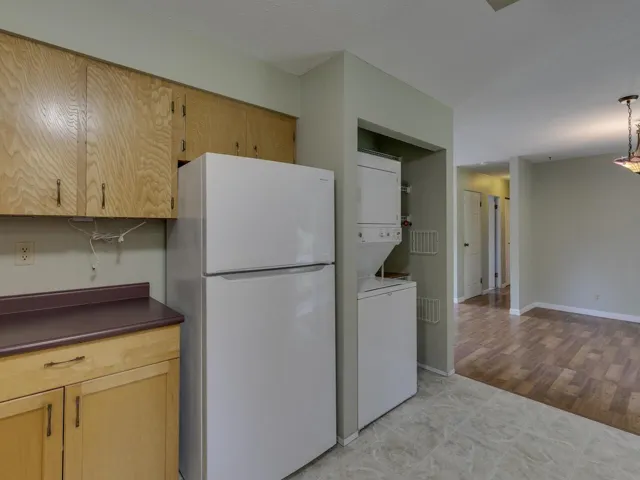 Kitchen featuring freestanding refrigerator, dark countertops, estacked washer and dryer, light brown cabinetry, and pendant lighting