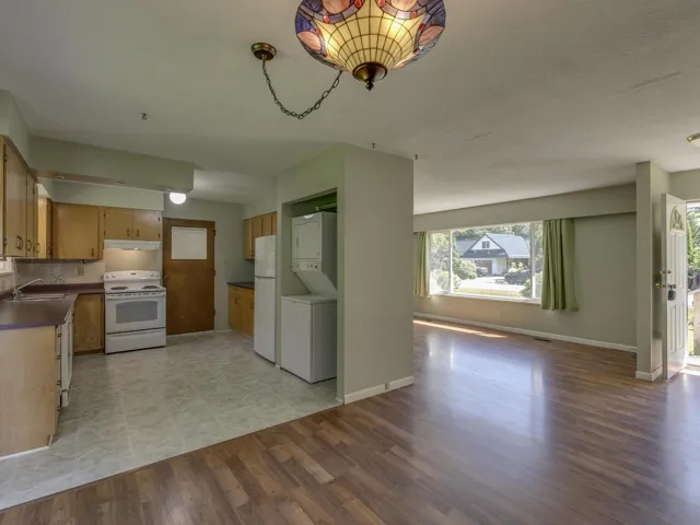 Kitchen with white appliances, dark countertops, stacked washer / drying machine, open floor plan, and light wood finished floors