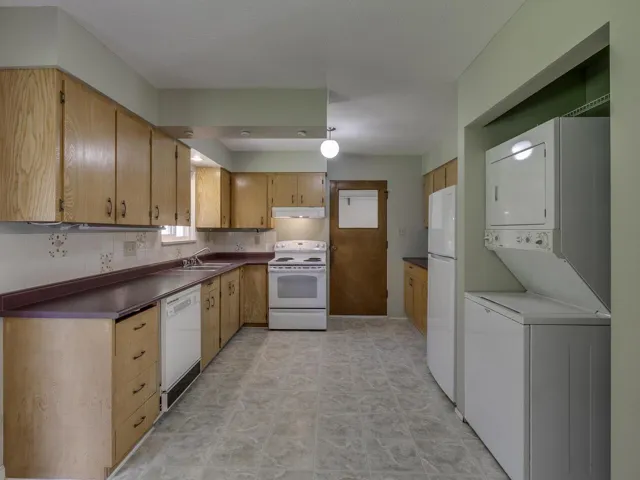 Kitchen featuring white appliances, dark countertops, stacked washer and clothes dryer, and under cabinet range hood