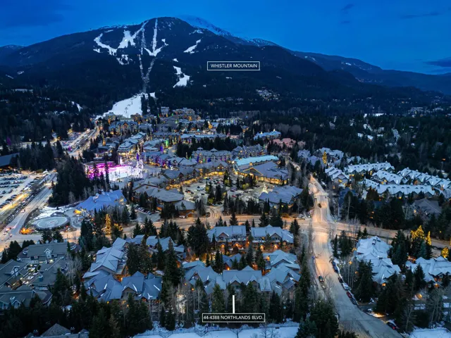 Aerial perspective of a mountain community featuring multiple residential and commercial structures, snow-covered landscapes, and illuminated streets
