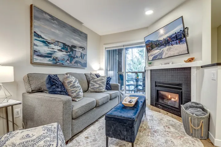 Living area featuring a tiled fireplace with white mantle, wood-finish flooring, recessed lighting, and a glass door providing access to an outdoor patio with metal railing
