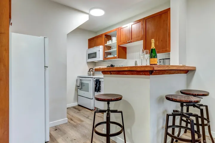 Kitchenette featuring a breakfast bar with wood-finish countertop, wood-finish cabinetry, white appliances, and wood-finish flooring