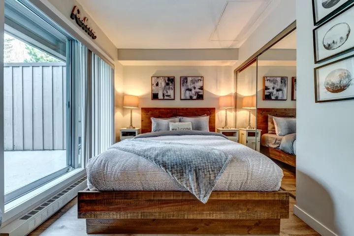 Bedroom featuring a wide sliding glass door opening to a private patio space, wood-finish flooring, mirrored closet doors, and a wood-paneled headboard