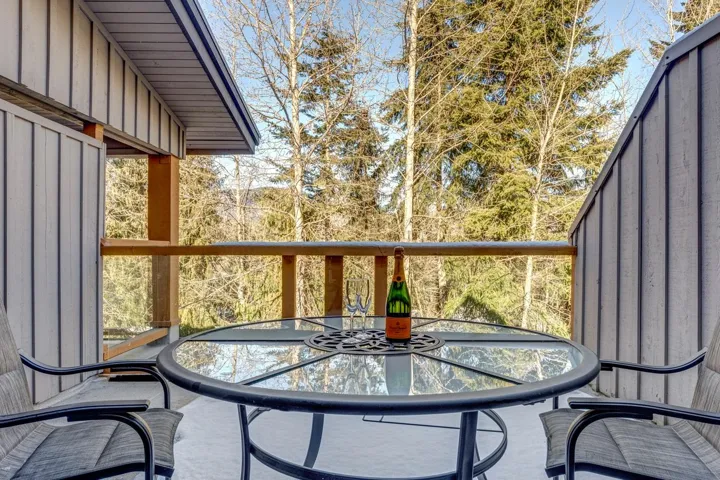 Private balcony with vertical panel siding, wood railing, and a glass-top table