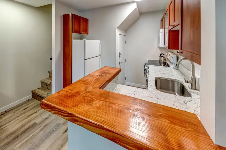 Kitchenette featuring a wood-finish bar, stainless steel sink with a modern faucet, stone-look countertops, and wood cabinetry