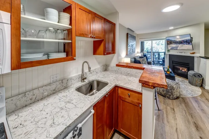 Kitchen featuring wood cabinetry, a stainless steel sink with a gooseneck faucet, light-toned countertops, and a white tile backsplash