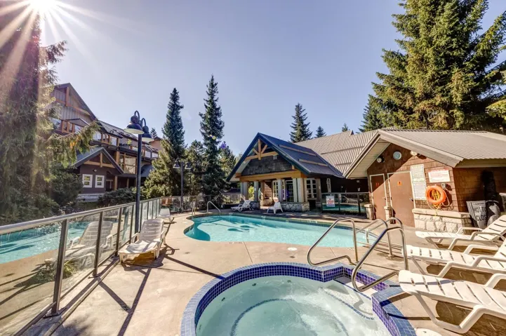 Outdoor swimming pool with integrated hot tub, surrounded by a concrete deck and glass panel railing