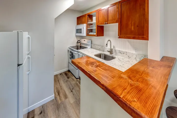Compact kitchen featuring a custom wood bar top, wood-finish cabinetry, white subway tile backsplash, and stone-finish countertops