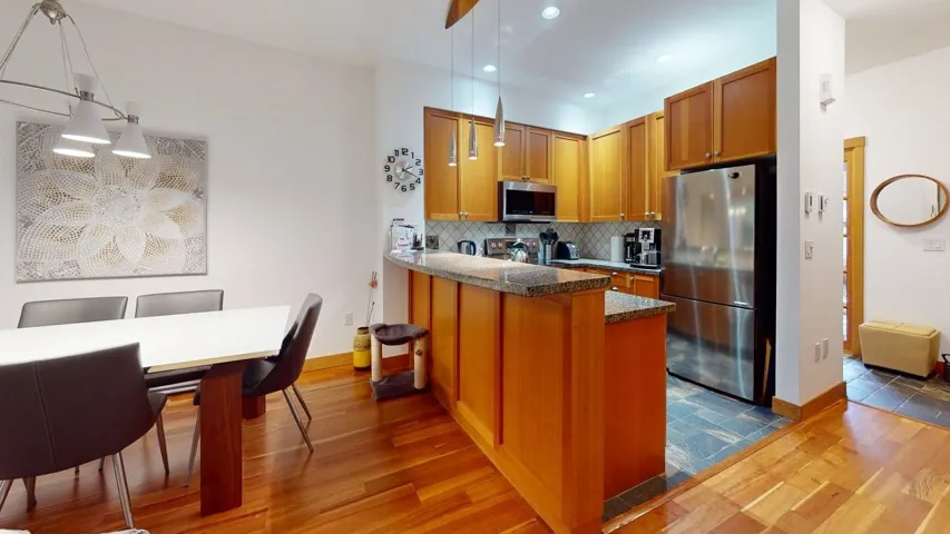 Kitchen with dark wood finished floors, appliances with stainless steel finishes, hanging light fixtures, a peninsula, and brown cabinets