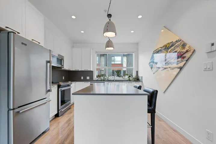 Kitchen with light wood finished floors, stainless steel appliances, white cabinets, tasteful backsplash, and a center island