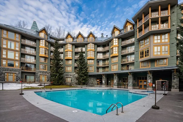 Outdoor swimming pool with concrete decking, surrounded by a multi-story building featuring stone veneer accents, wood-frame windows, and private balconies