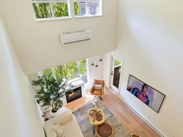 Living room with a high ceiling, a baseboard radiator, a glass covered fireplace, wood finished floors, and a wall mounted AC