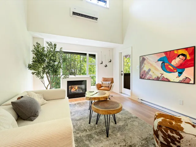 Living room with light wood-style floors, an AC wall unit, a towering ceiling, and a glass covered fireplace