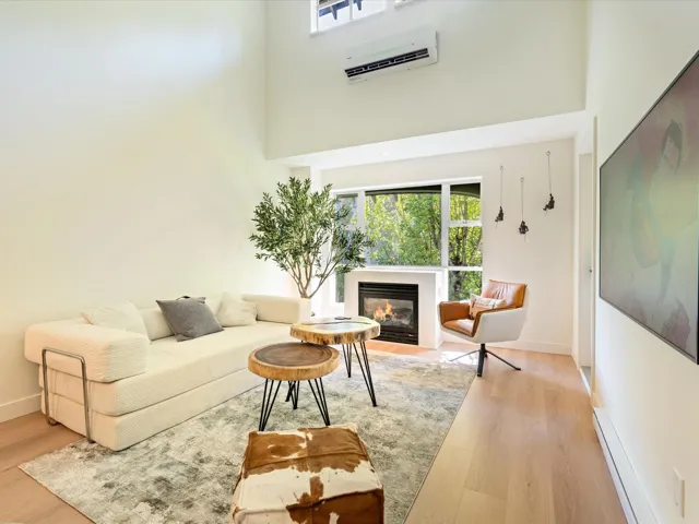 Living area featuring baseboard heating, a wall unit AC, light wood-style floors, a high ceiling, and a glass covered fireplace