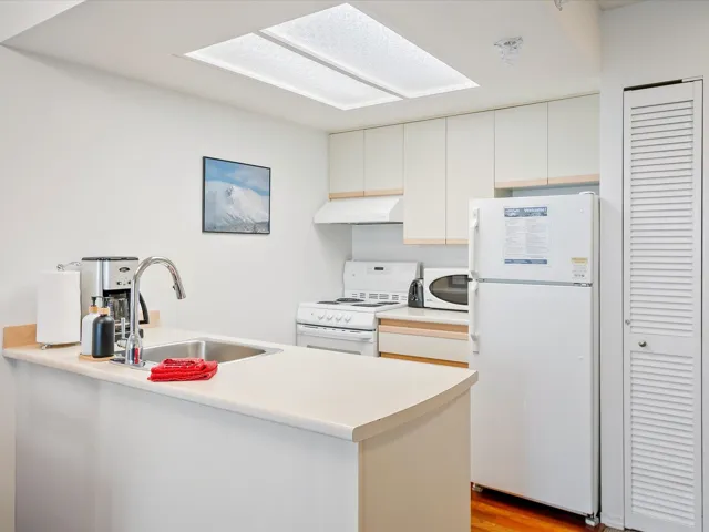 Kitchen featuring white appliances, light countertops, a peninsula, light wood-type flooring, and under cabinet range hood