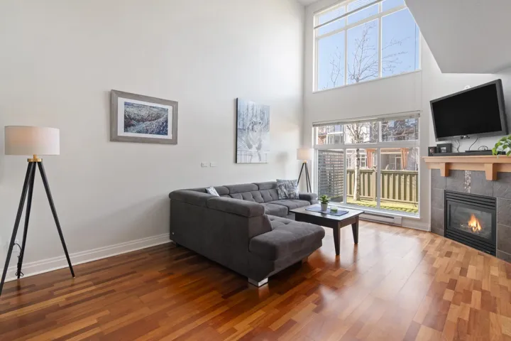 Living room with a towering ceiling, a tile fireplace, baseboards, and wood finished floors
