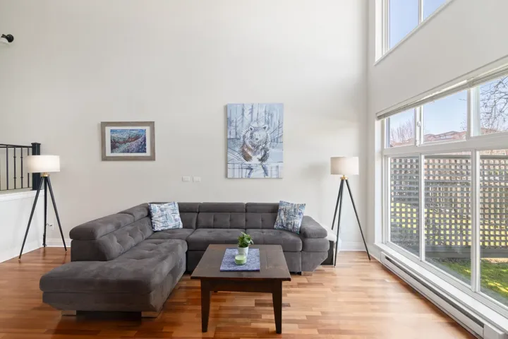 Living room with a baseboard heating unit, a healthy amount of sunlight, a towering ceiling, and light wood finished floors