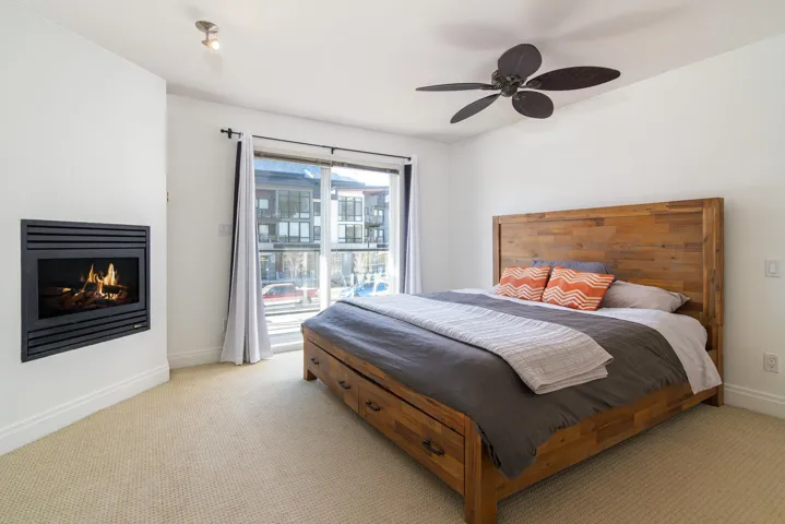 Bedroom featuring baseboards, ceiling fan, a lit fireplace, access to exterior, and light colored carpet