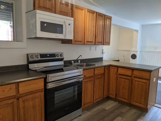Kitchen with a sink, dark countertops, white microwave, and electric stove