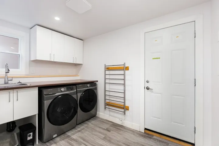 Clothes washing area with light wood finished floors, baseboards, cabinet space, a sink, and washing machine and dryer