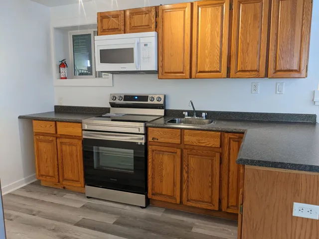 Kitchen with a sink, stainless steel range with electric stovetop, brown cabinets, dark countertops, and white microwave