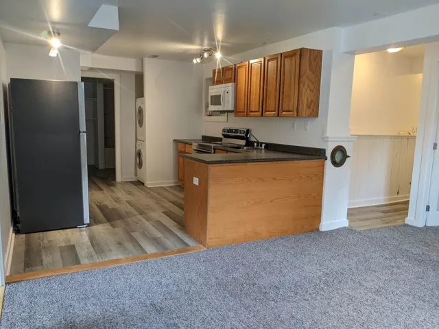 Kitchen featuring stacked washer / drying machine, a sink, appliances with stainless steel finishes, brown cabinetry, and dark countertops