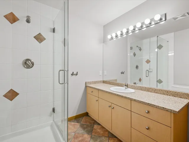 Bathroom with vanity, a shower stall, and dark stone finish floors