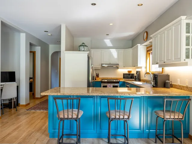 Kitchen featuring blue cabinetry, arched walkways, light wood-style floors, light stone countertops, and recessed lighting