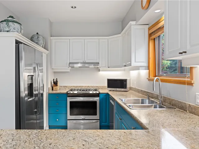 Kitchen featuring white cabinets, stainless steel appliances, under cabinet range hood, blue cabinetry, and recessed lighting