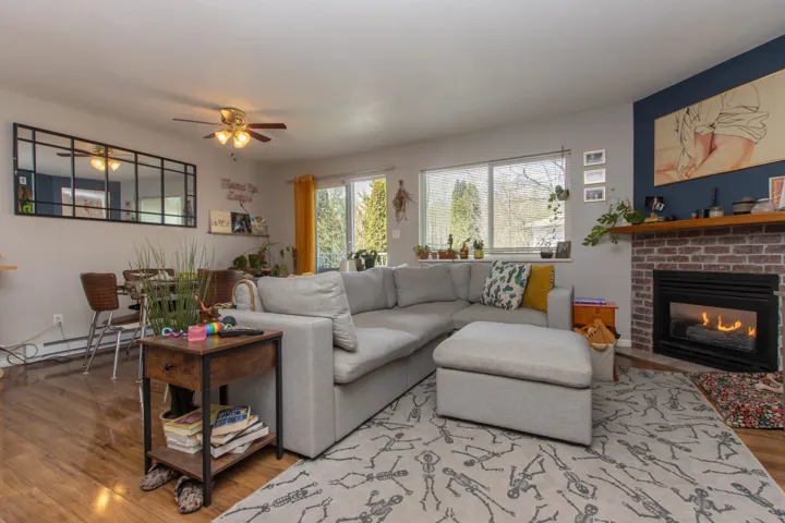 Living area featuring a baseboard heating unit, ceiling fan, light wood-style floors, and a fireplace