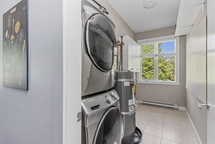 Dedicated laundry space featuring a window, tiled flooring, stacked appliances, and built-in white cabinetry