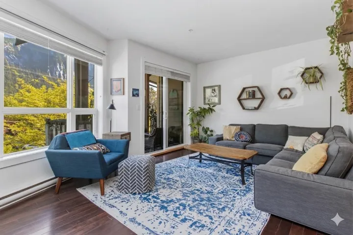 Spacious living area featuring large windows, wood-finish flooring, white walls, and built-in shelving