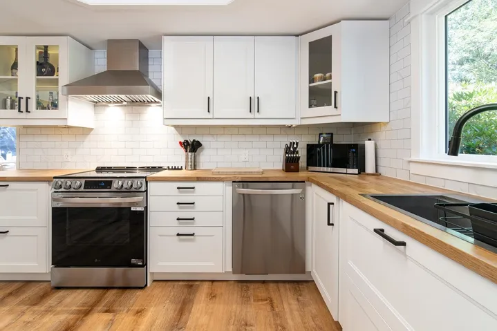 Kitchen featuring wooden counters, wall chimney range hood, appliances with stainless steel finishes, and plenty of natural light