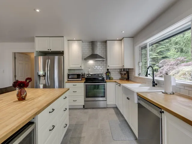 Kitchen featuring butcher block countertops, wall chimney exhaust hood, appliances with stainless steel finishes, decorative backsplash, and wine cooler