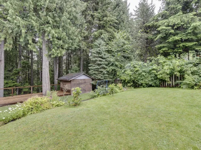 View of green lawn with a wooden deck and a storage shed