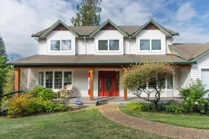 View of front of home with covered porch, roof with shingles, a front yard, and a garage