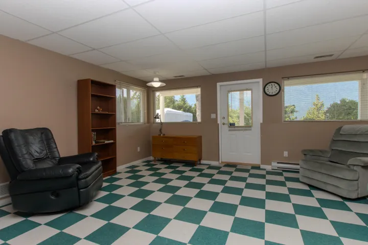 Living area with a drop ceiling, a baseboard heating unit, and light floors