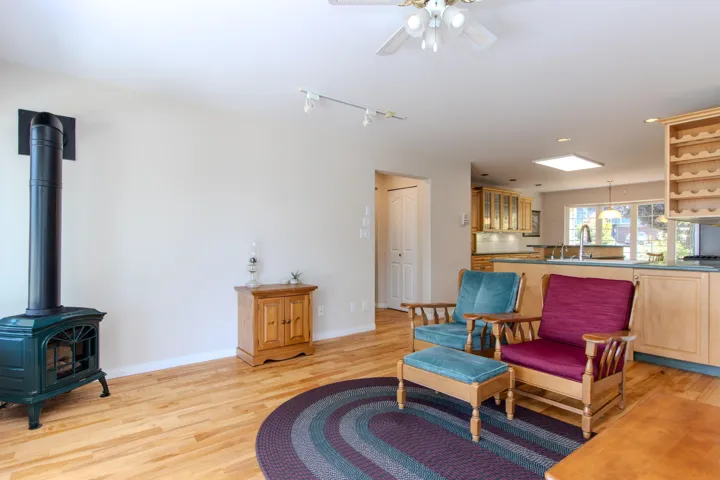 Sitting room with light wood-style flooring, a wood stove, ceiling fan, and rail lighting