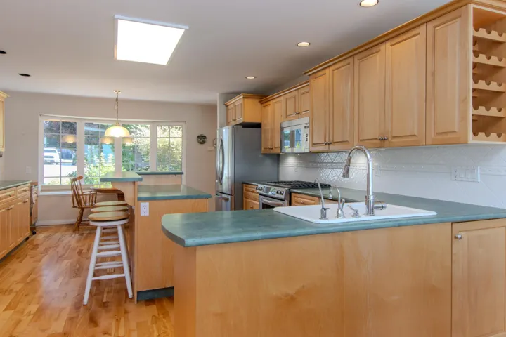Kitchen featuring a kitchen island, backsplash, light wood-style flooring, stainless steel appliances, and decorative light fixtures