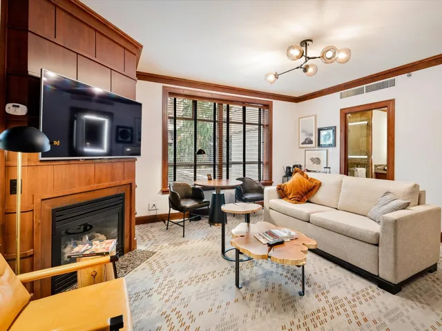 Living room featuring a glass covered fireplace, ornamental molding, visible vents, a chandelier, and baseboards