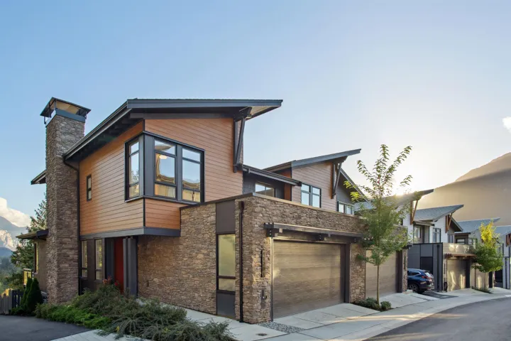 Modern home with stone siding, an attached garage, driveway, and a chimney