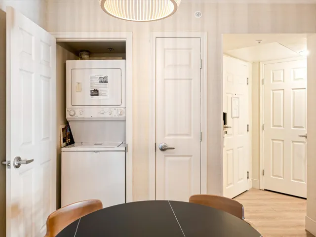 Laundry room with wallpapered walls, light wood-type flooring, and stacked washing machine and dryer