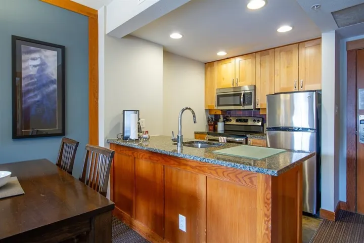 Kitchen featuring stainless steel appliances, a sink, a peninsula, recessed lighting, and dark stone countertops